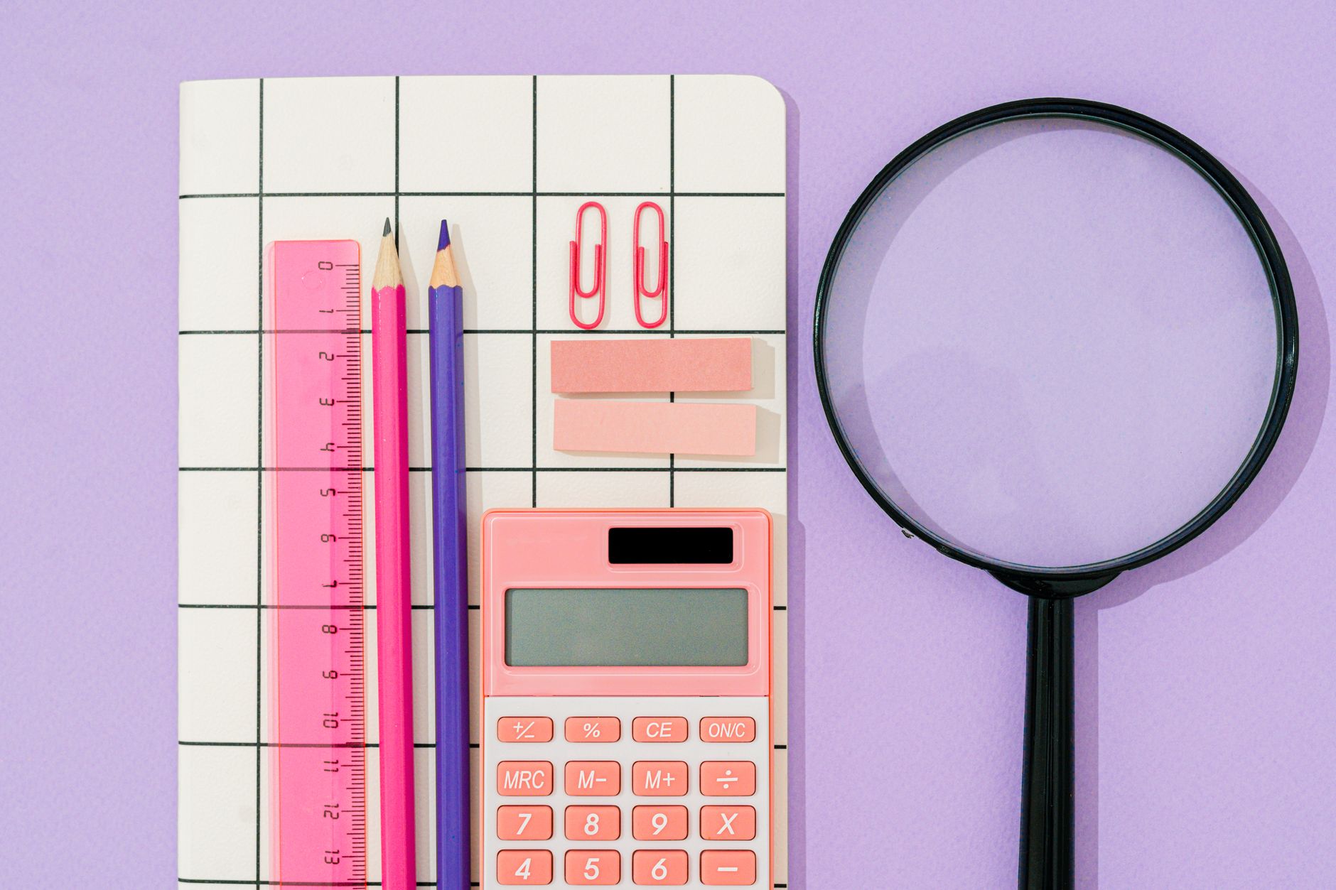 Flat lay of pastel office supplies on a grid notebook with purple background.