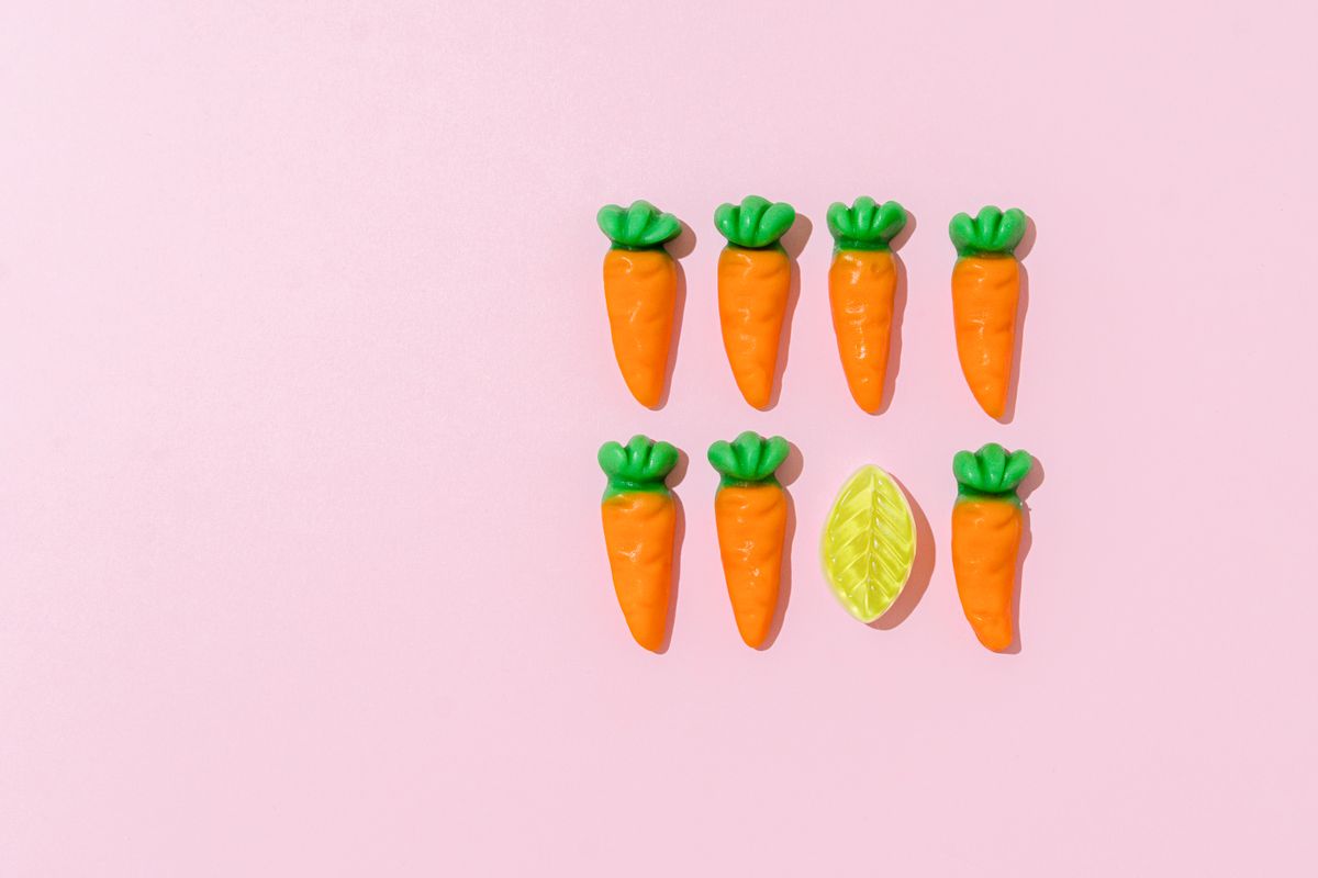 Vibrant gummy carrots with a leaf on a pastel pink background, perfect for sweets and treats imagery.