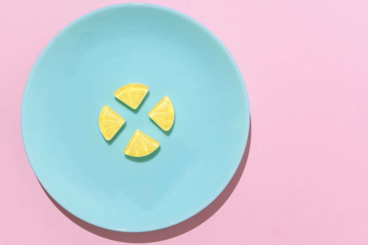 Lemon-shaped candies arranged on a blue ceramic plate against a pink background.
