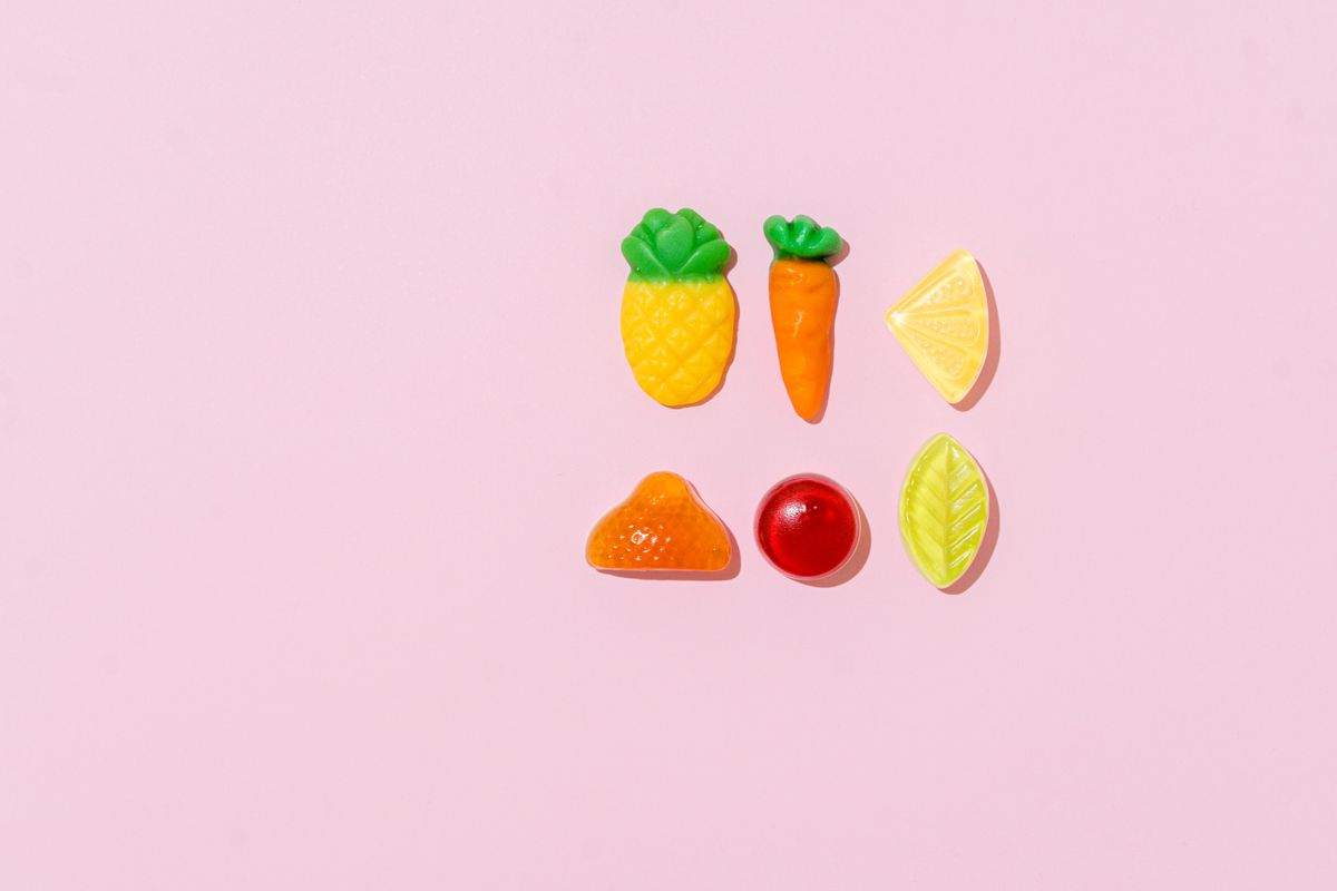 Top view of assorted fruit-shaped candies on a pastel pink background.