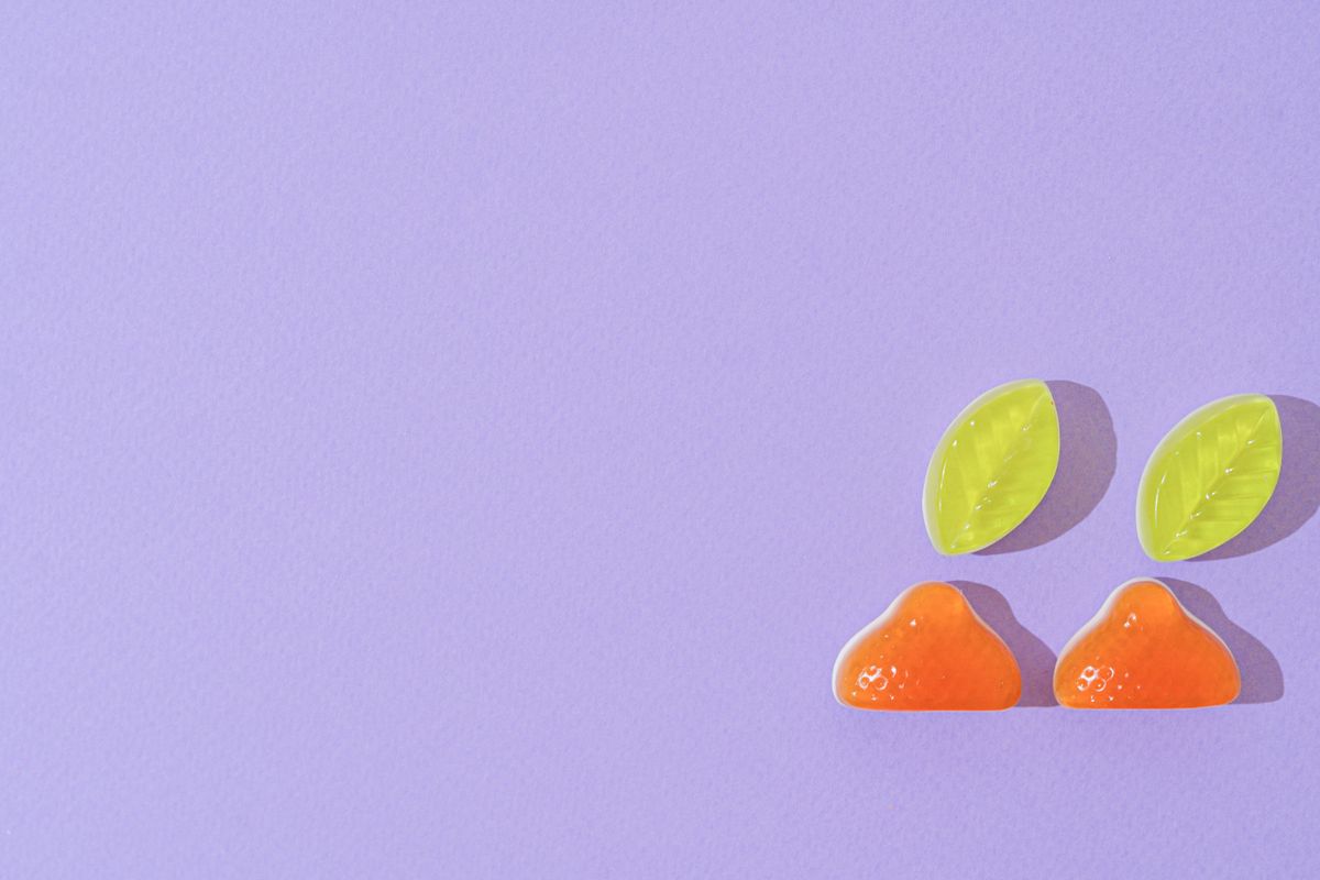 Vibrant orange and green jelly candies shaped as fruits cast shadows on a purple backdrop.