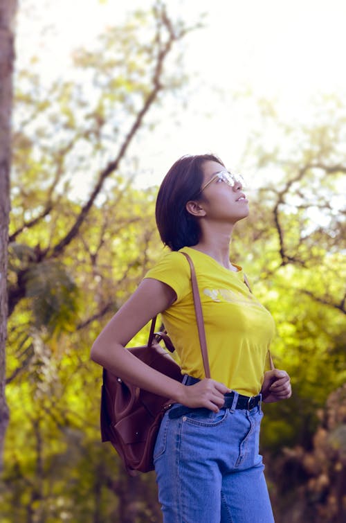 Женщина в желтой рубашке смотрит вверх в окружении деревьев