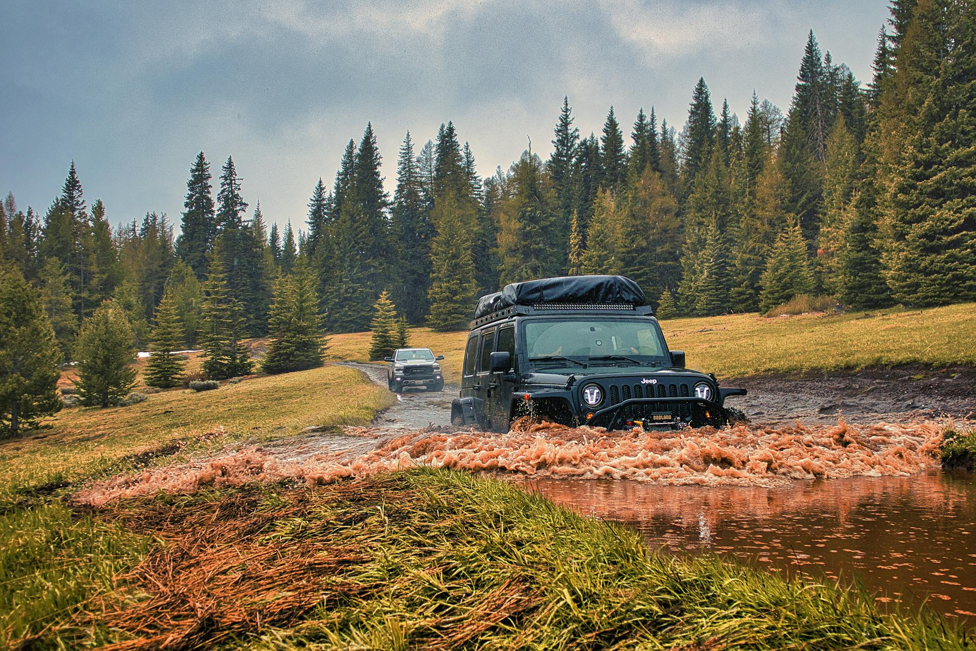 Jeep traversing a muddy off-road trail in a scenic forest. Ideal for adventure enthusiasts.