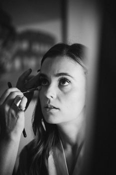 Grayscale close-up of a woman having makeup applied, showcasing artistry and concentration.
