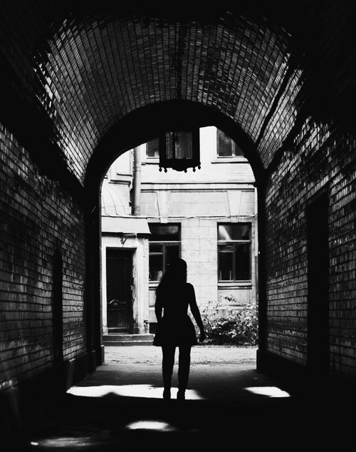 Free Moody black and white silhouette of a woman walking through a tiled urban tunnel. Stock Photo