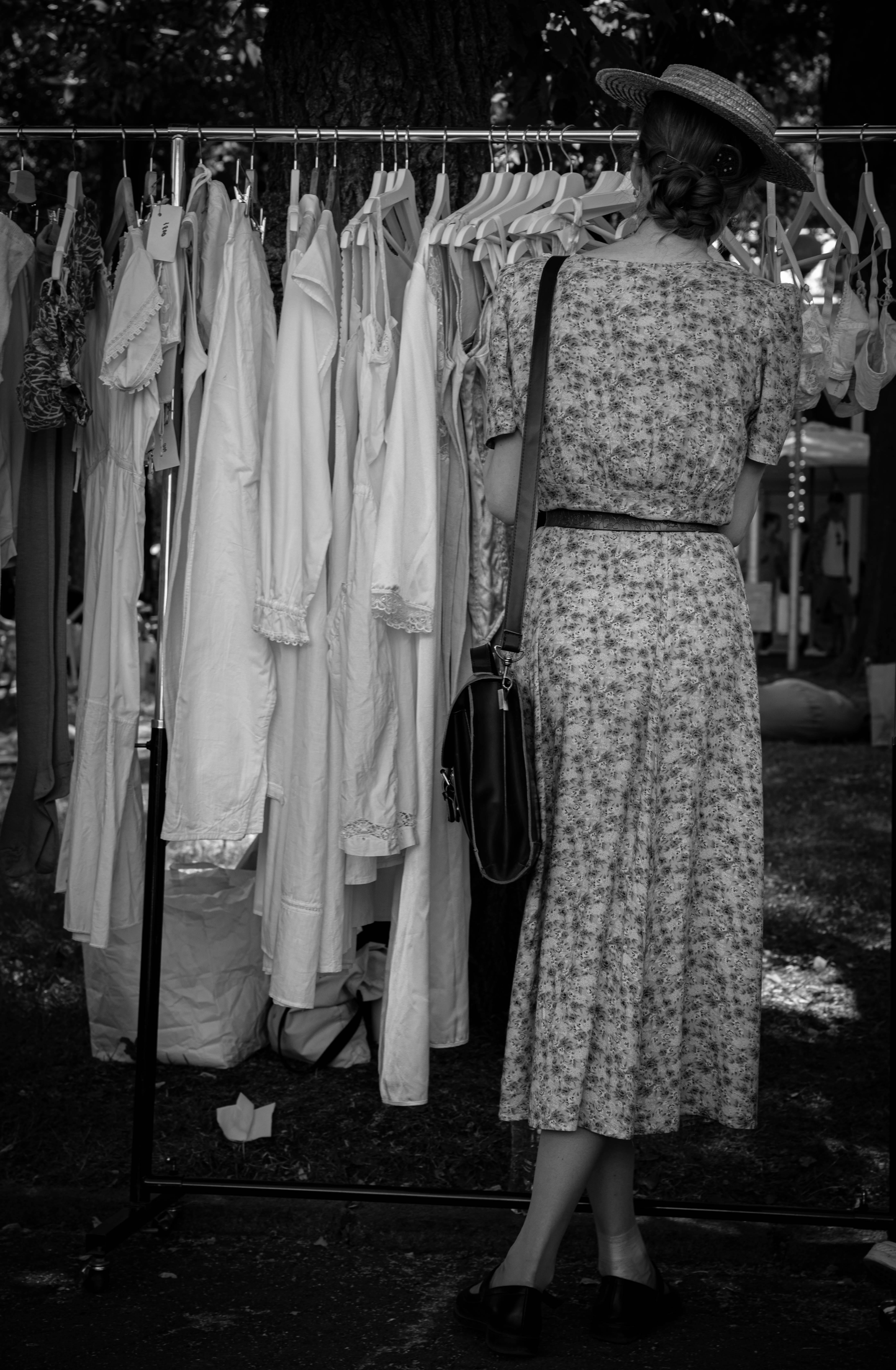 A woman in vintage attire explores clothes at an outdoor market, embracing retro fashion.
