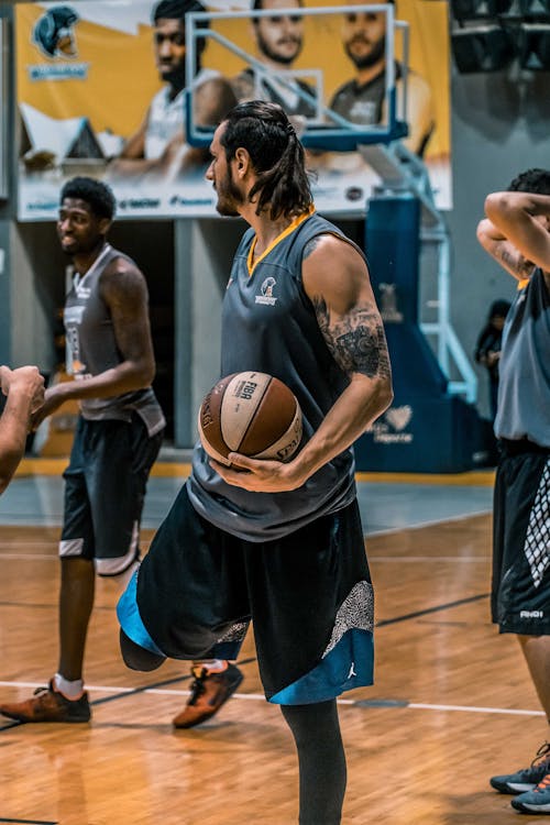 Uomo In Camicia Senza Maniche Grigia Che Trasporta Pallacanestro Spalding Bianco E Marrone