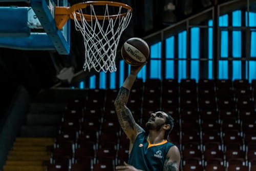 grátis Homem Segurando Uma Bola De Basquete Spalding Branca E Preta Perto De Uma Cesta De Basquete Marrom E Branca Foto profissional