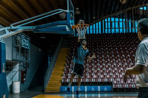 Free Man in Blue Shirt Trying to Dunk in Basketball Ring Stock Photo