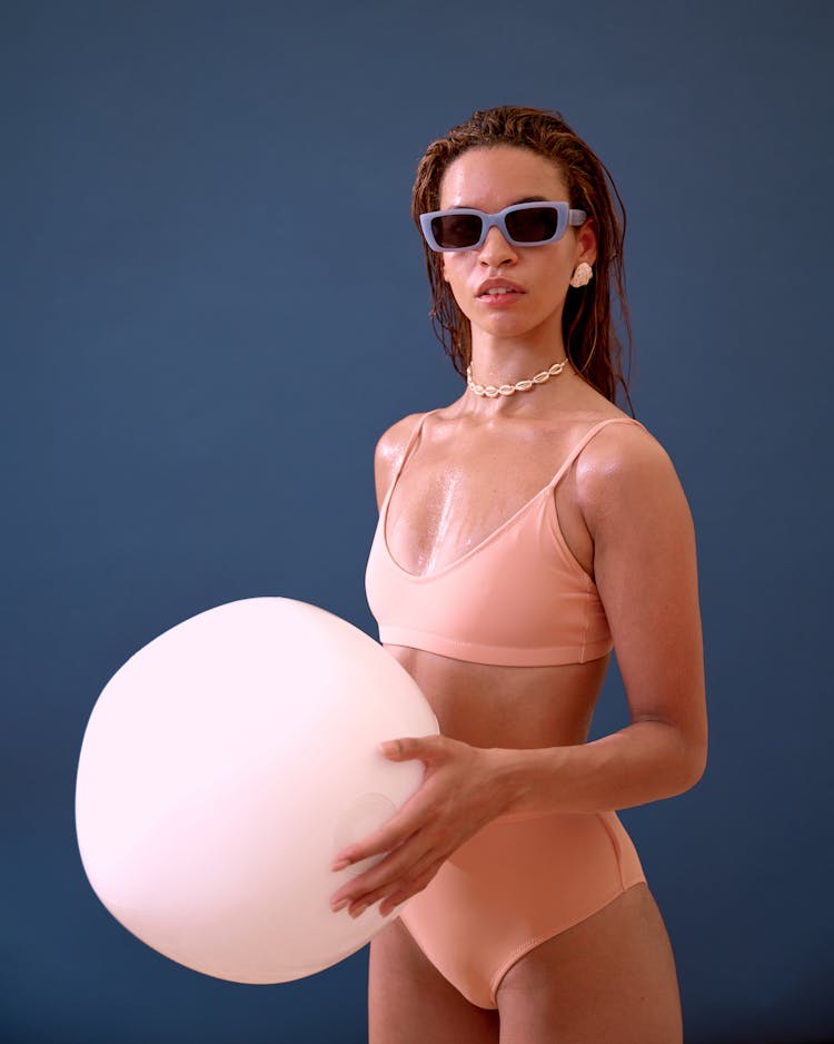 A Woman In Pink Bikini Wearing Sunglasses Holding A Pillow