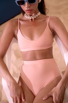 Woman in pink swimwear wearing sunglasses and shell choker relaxing outdoors.