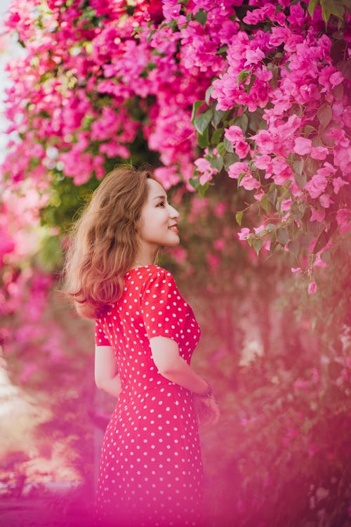 Woman in Red Polka Dot Dress Standing Near a Pink Flowering Tree
