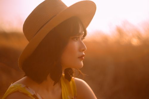 Free A serene side profile of a woman in a straw hat, captured at sunset for a warm, dreamy mood. Stock Photo