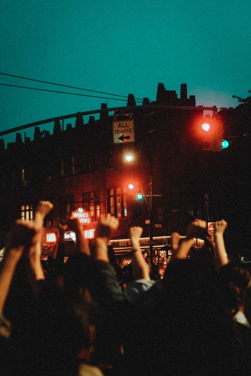 Free Dramatic night scene of a crowd raising fists beneath vibrant city traffic lights. Stock Photo