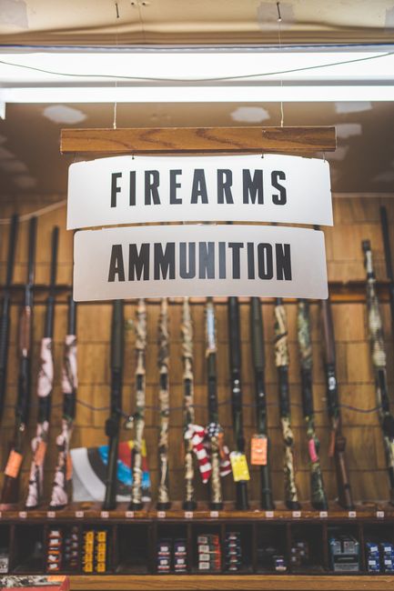 Fotomural Cartel en una tienda de armas y municiones que presenta rifles y productos relacionados.