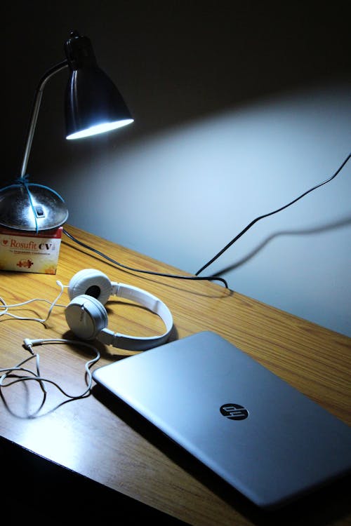 無料 茶色の木製テーブルに灰色のhpノートパソコンと白いコード付きヘッドフォン 写真素材