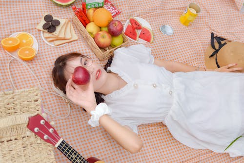 Free A Pretty Woman Lying on a Checkered Blanket Holding an Apple on Her Face Stock Photo