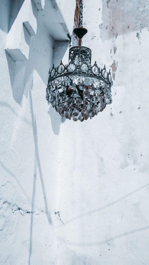 Free A vintage crystal chandelier hanging against a weathered white wall, casting unique shadows. Stock Photo