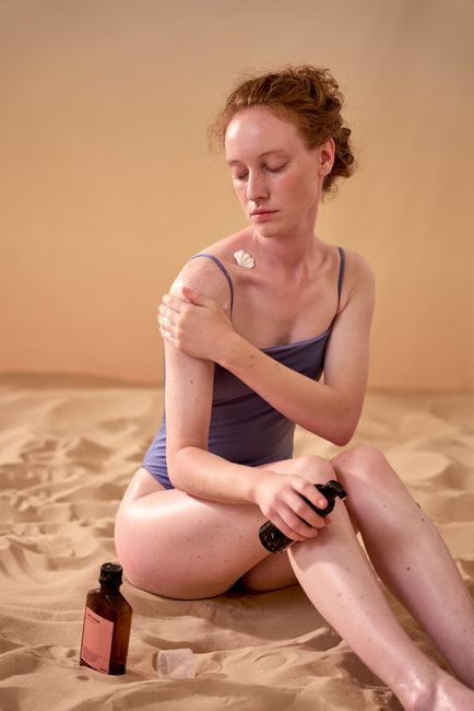 Caucasian woman applying sunscreen while sitting on sand, embodying skin protection and self-care.