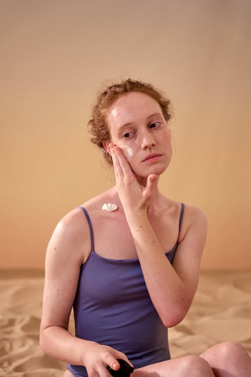 Woman in Blue Swimwear Applying Cream on Her Face 