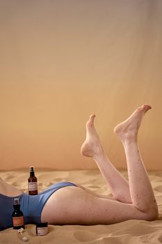 A woman applying skincare products while relaxing on a sandy beach.