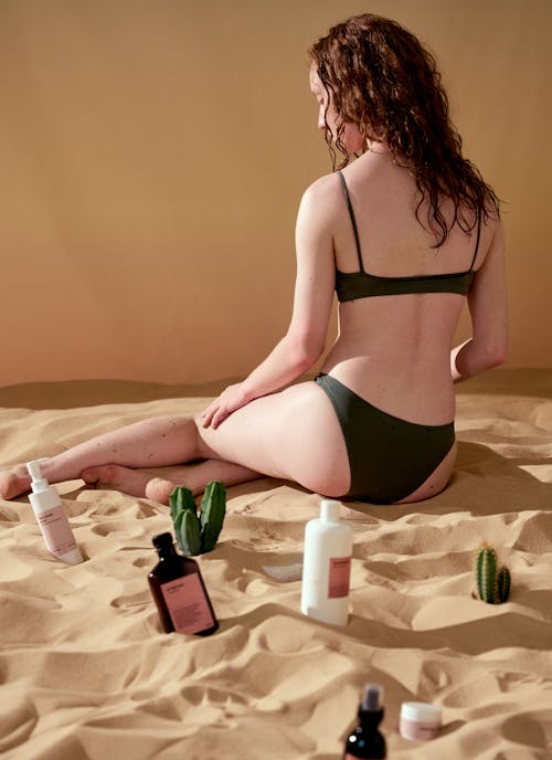 Woman in Black Bikini and Cosmetic Products on a Beach Sand