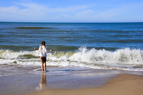 Free A young girl enjoying ocean waves on a sunny beach day, symbolizing freedom and adventure. Stock Photo