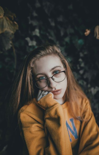 Close-up portrait of a woman in glasses wearing a yellow sweater outdoors.