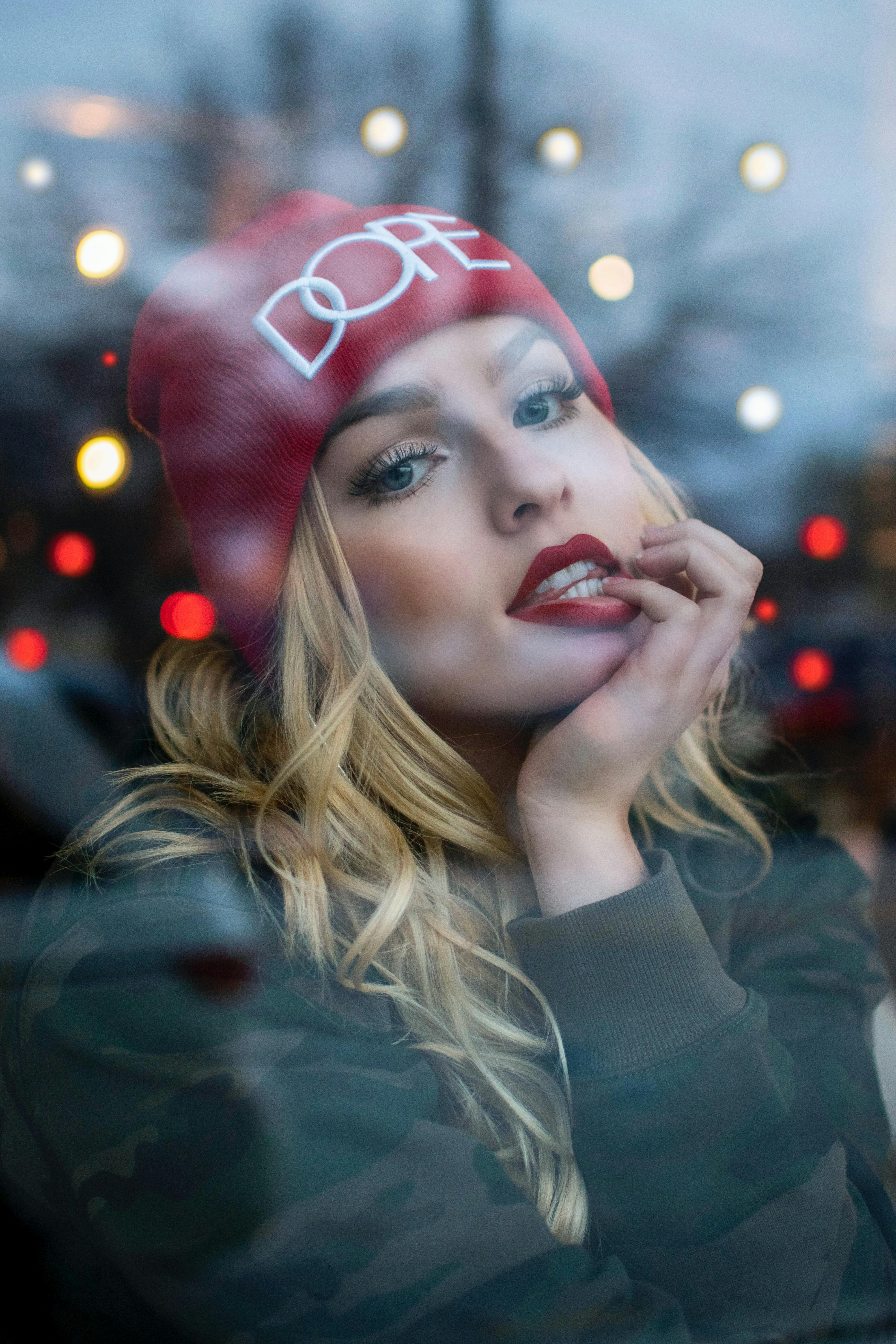 Portrait of a woman in a red beanie gazing through a window with bright bokeh lights.