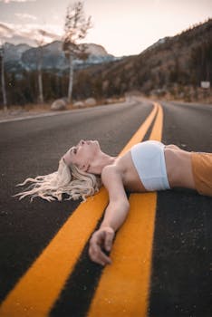A young woman lies carefree on a mountain road, embracing freedom under a sunset sky.