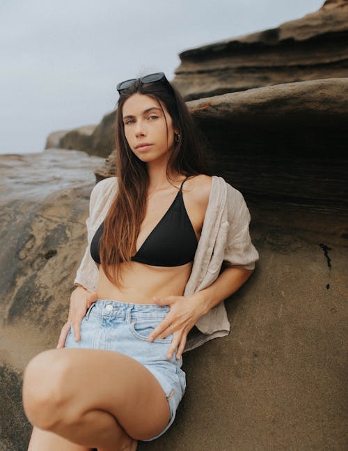 Young woman posing on stones and wearing jeans shorts and bikini