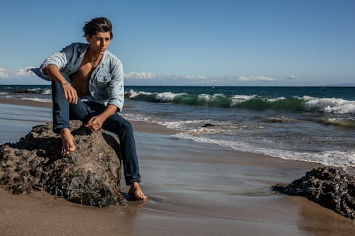 Free A Man Sitting on a Rock at the Beach  Stock Photo