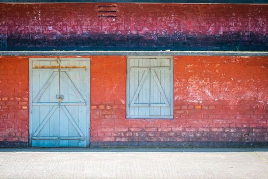 A bright red brick wall with a blue wooden door and window, showcasing rustic charm.