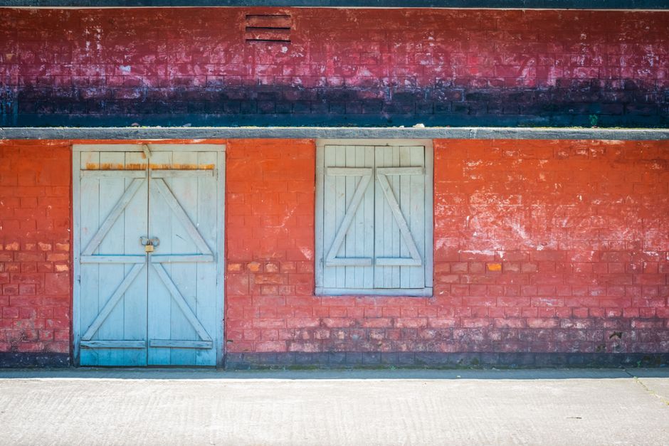 A bright red brick wall with a blue wooden door and window, showcasing rustic charm.