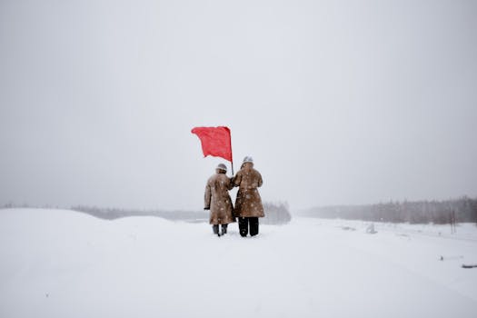 Two figures stand in a snowy landscape holding a red flag, symbolizing protest and revolution.