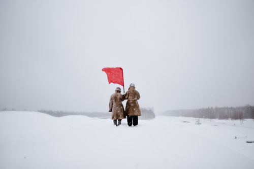 Free Two figures stand in a snowy landscape holding a red flag, symbolizing protest and revolution. Stock Photo