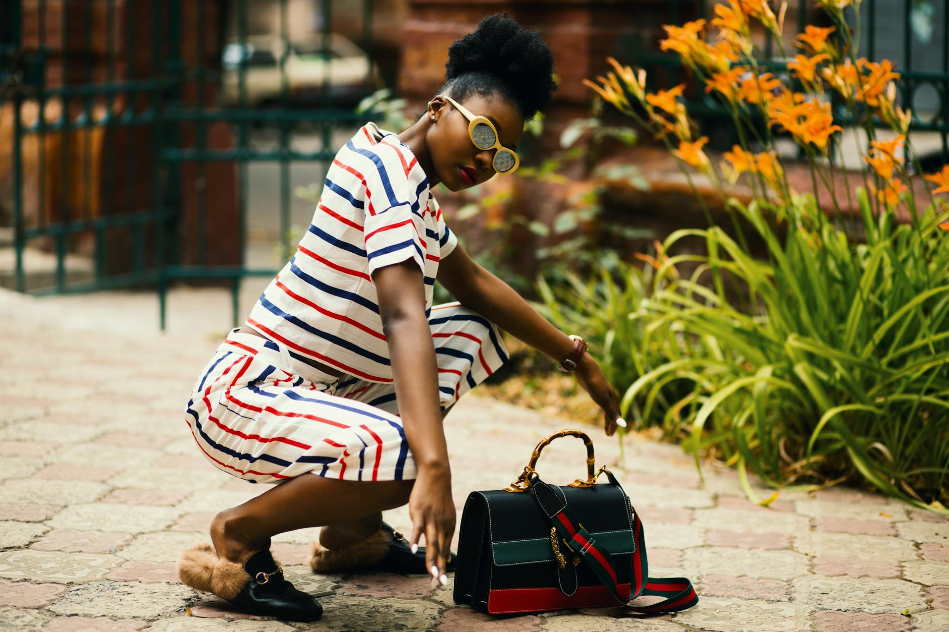 Stylish woman squatting outdoors with trendy striped outfit and designer bag. Vibrant and fashionable.