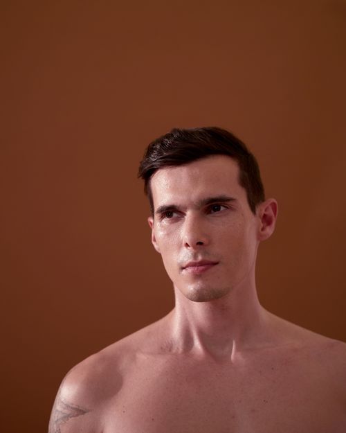 Free Close-up portrait of a topless young man against a brown background. Stock Photo