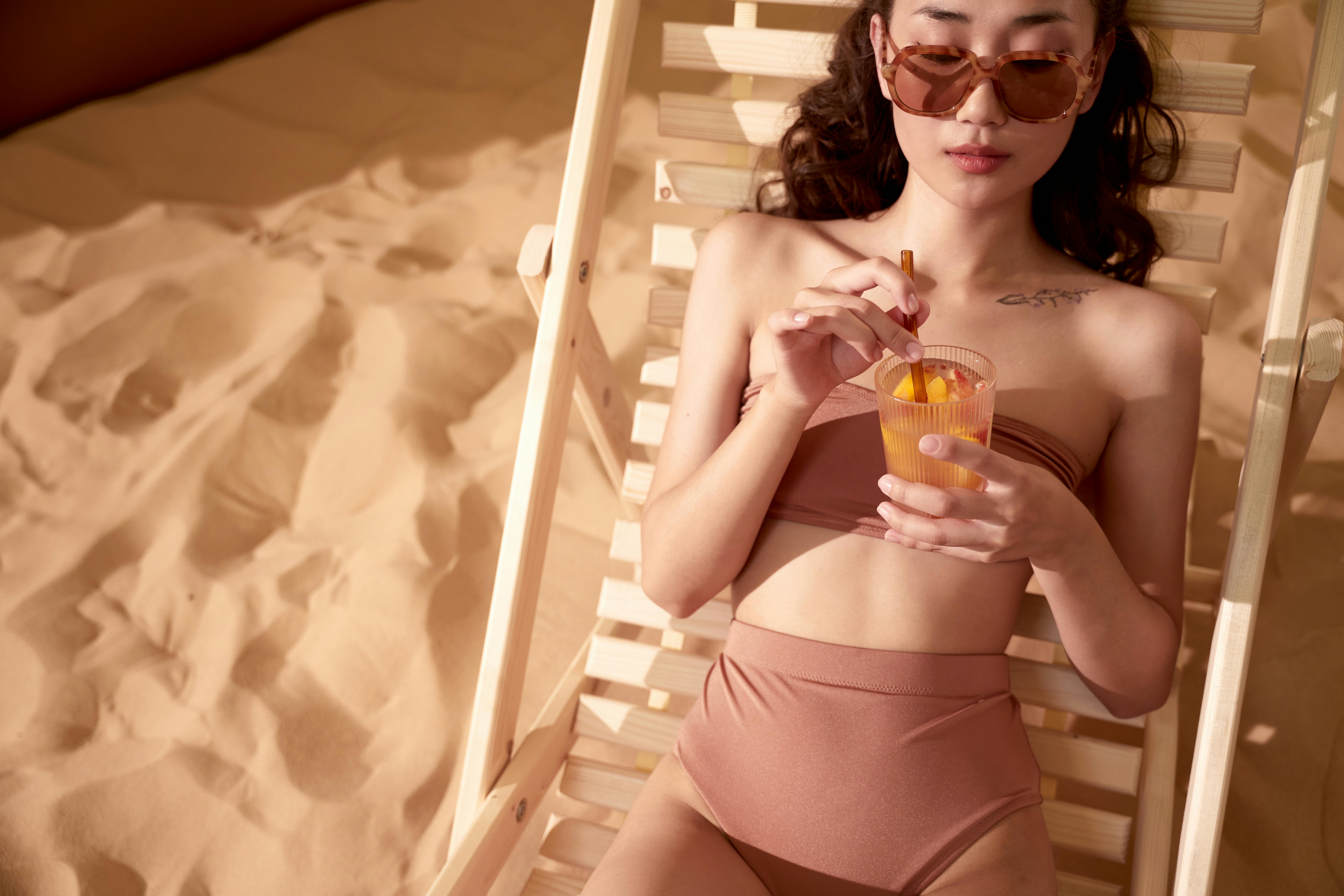 Woman in swimwear enjoying a refreshing drink on a sunny day. Perfect summer vibe.