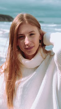 A young woman in a cozy white turtleneck sweater enjoys a day by the ocean.