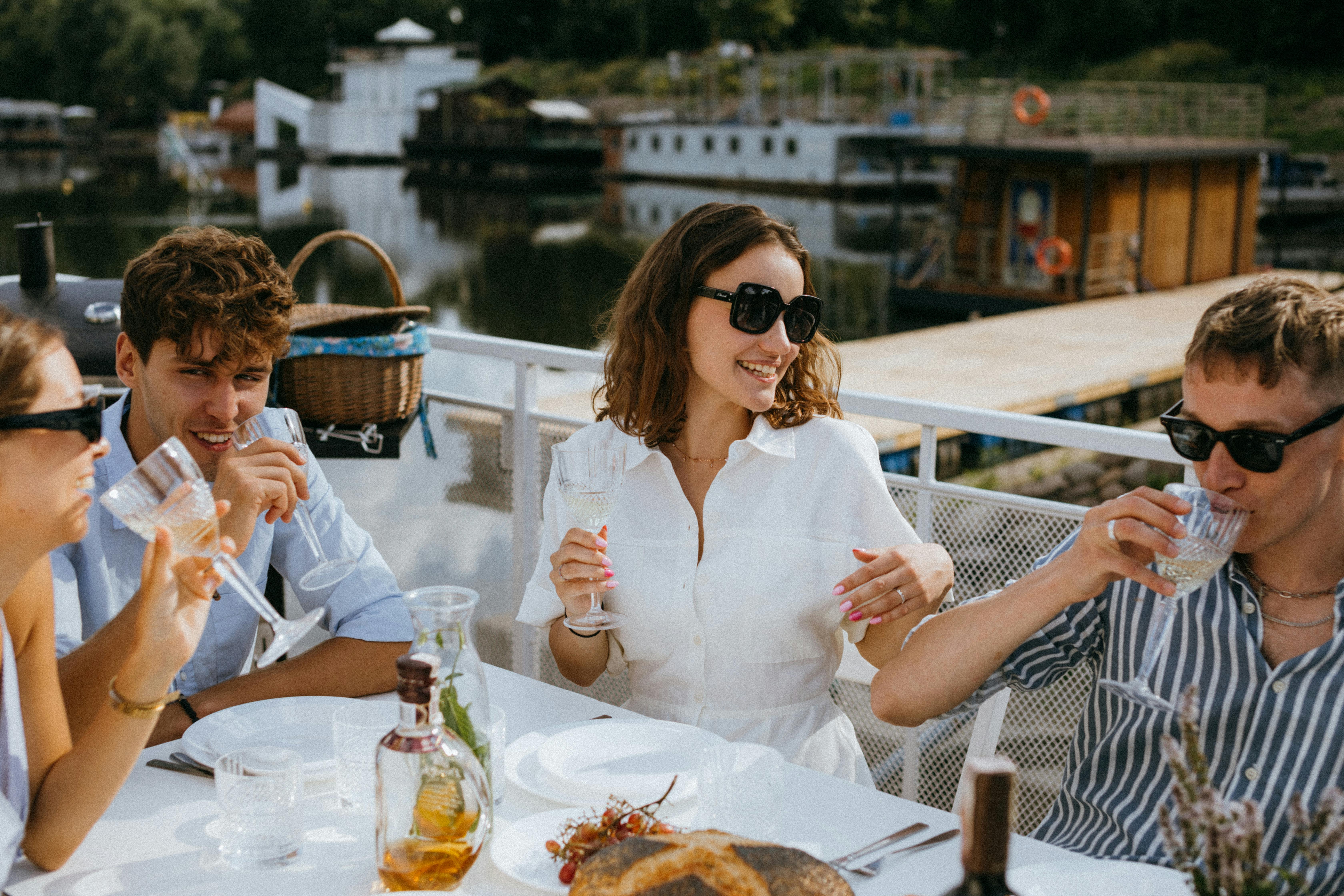 Group of friends enjoying drinks and laughter at a summer outdoor gathering by the water.