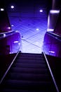 自动扶梯在鲜艳的紫色灯光映照下，呈现出戏剧性的镜头，营造出未来派的氛围