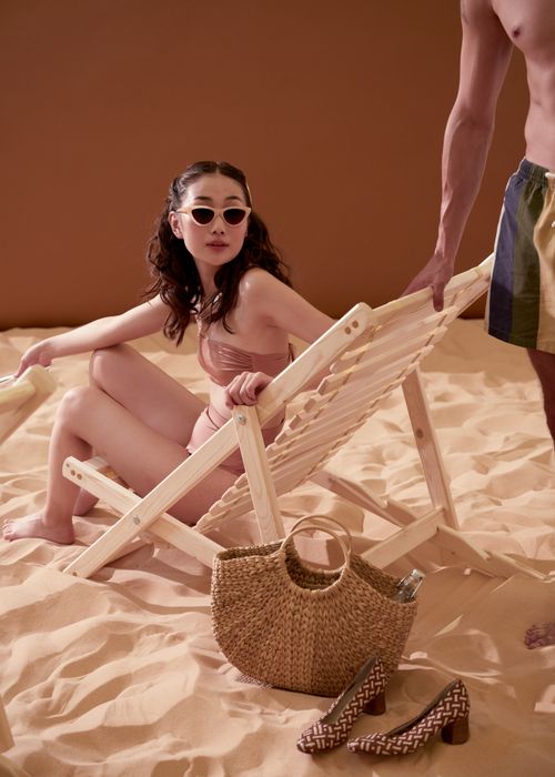 Free Woman in swimsuit relaxing on deck chair in a studio setup resembling a beach scene. Stock Photo
