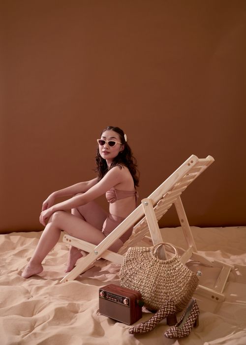 Free Elegant woman in swimsuit and sunglasses sitting on a beach chair with a retro vibe. Stock Photo