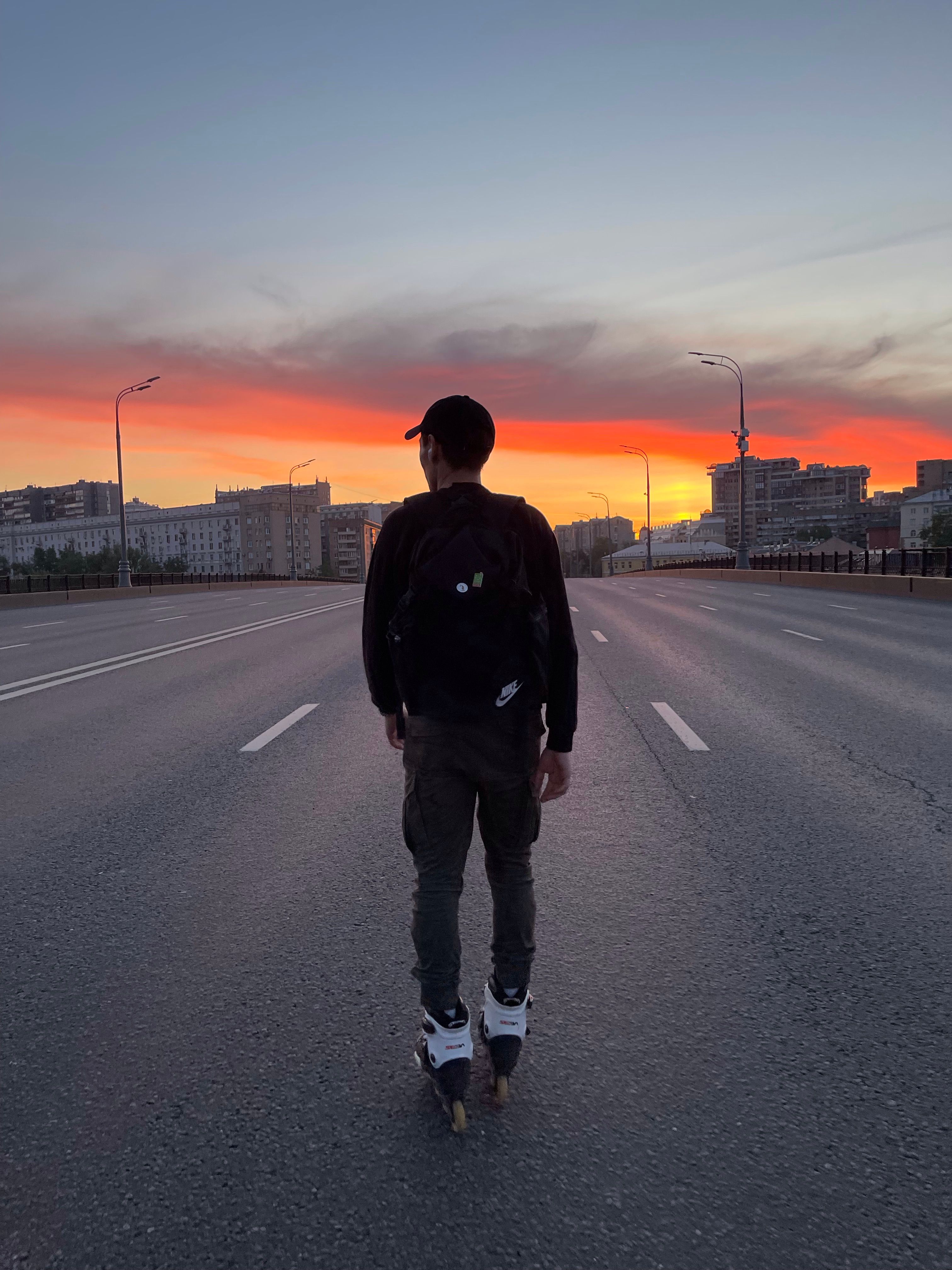A man rollerblades alone down an empty city street during a stunning sunset.
