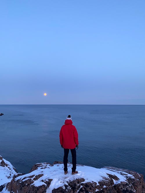 Person in Red Hoodie Jacket Standing on Rock with Snow