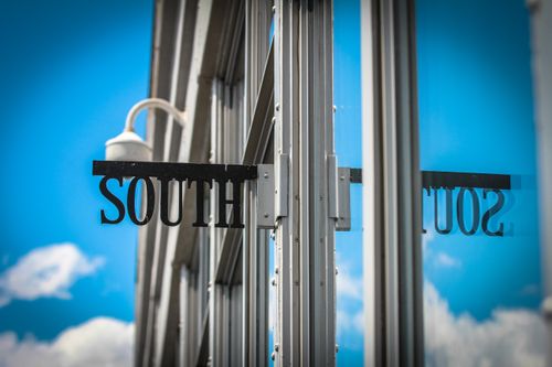 Free Reflection of 'South' sign on a glass building facade under clear blue skies. Stock Photo