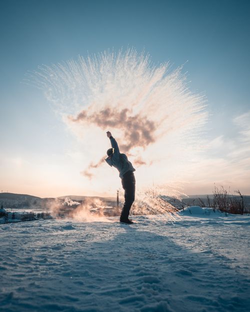 Free Person throwing hot water into cold air, creating an artistic snow effect at sunrise. Stock Photo