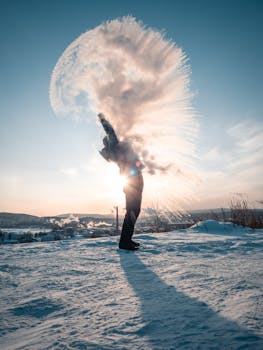 Silhouette of a person throwing snow in the air, backlit by the sun on a snowy landscape.