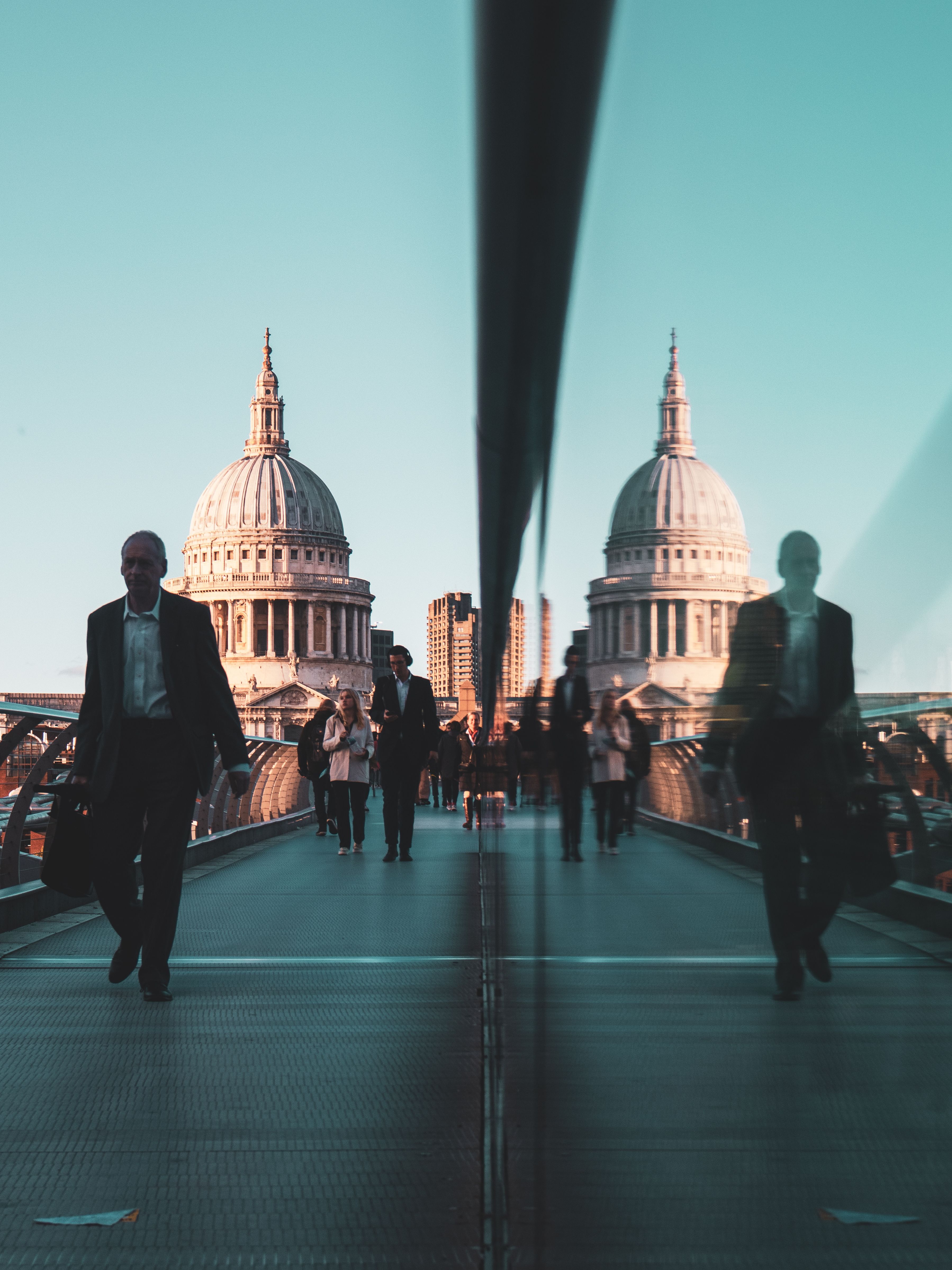 People walking on Millennium Bridge with a reflection of St Paul's Cathedral in London.